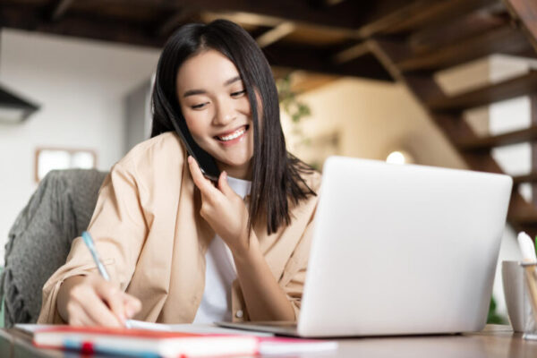 Smiling Asian Woman Working From Home Taking Notes Notebook Talking Cellphone Writing Down 768x512